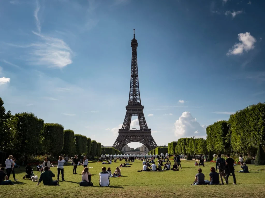 Utsikt over Eiffeltårnet en solfylt dag med folk som slapper av i en park i Paris.