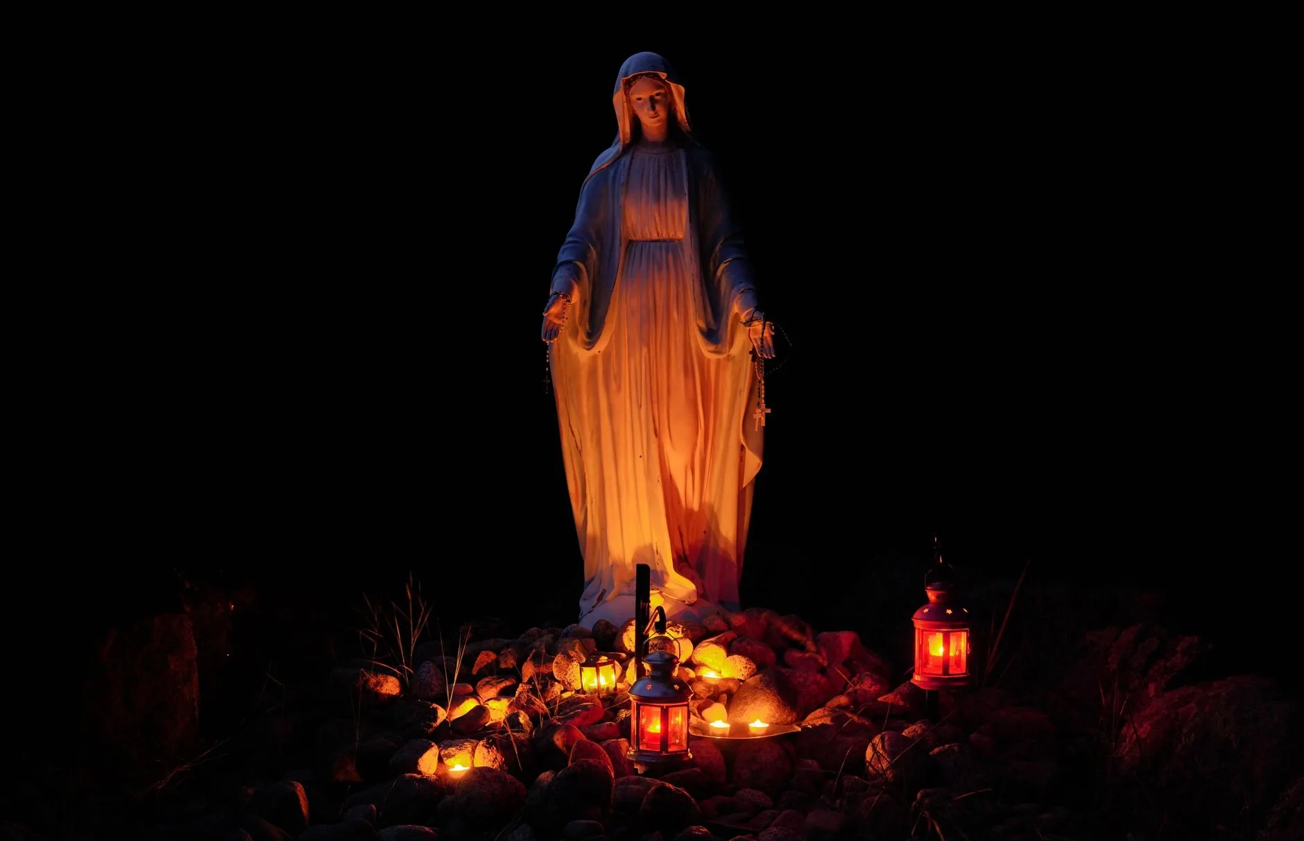 En staty av Jungfru Maria omgiven av levande ljus i mörkret.